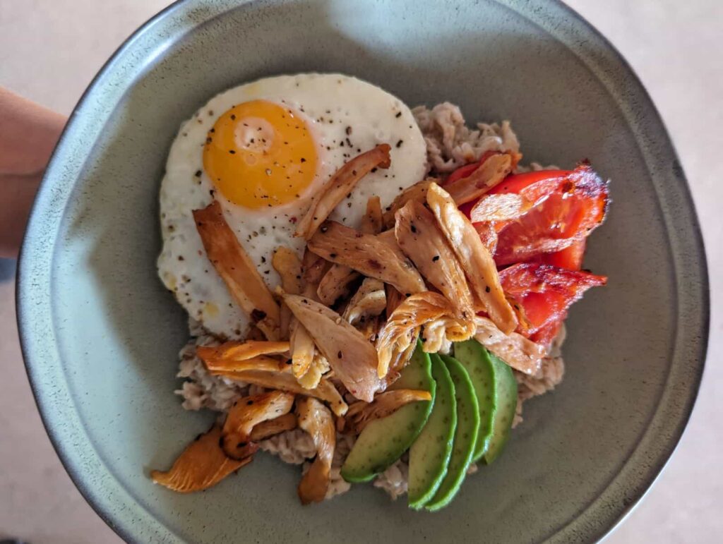 sūri avižinė košė su rožinės kreivabūdės grybais, keptu kiaušiniu, keptais pomidorais ir avokadu.